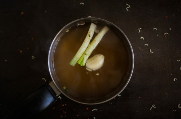 Comment faire des ramen maison: porter le bouillon à ébullition et ajouter une gousse d'ail, du gingembre pelé et des tiges d'oignon vert